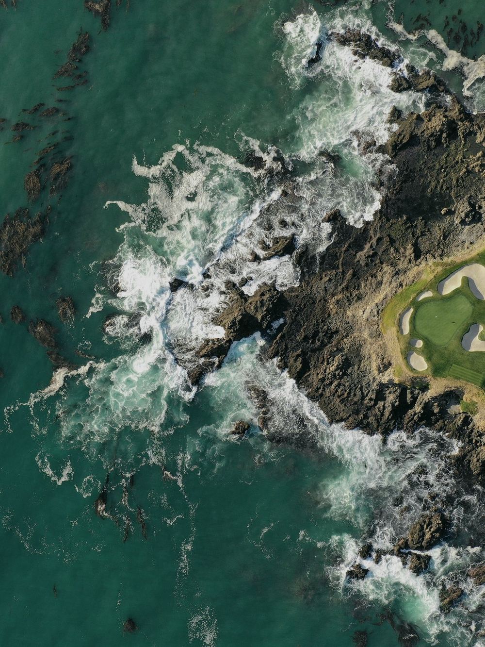 Aerial view of a coastal golf green ringed by rocks and breaking surf